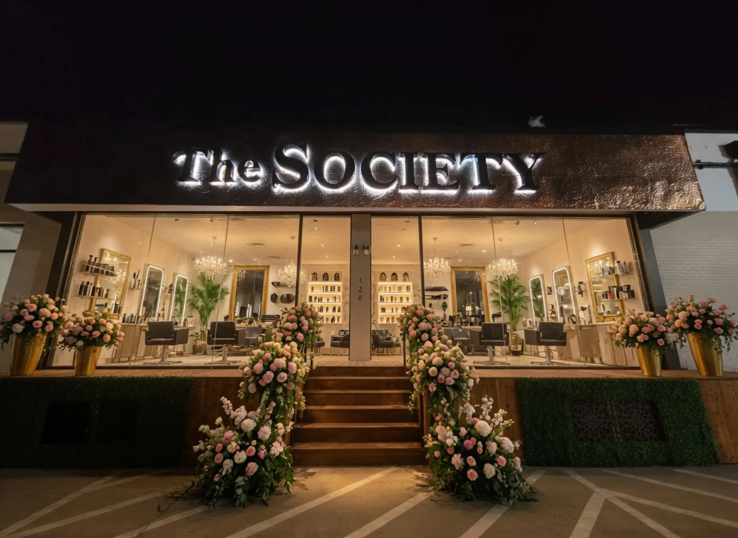 The Society salon storefront in Oak Lawn, Dallas, lit at night with floral arrangements framing the entrance steps